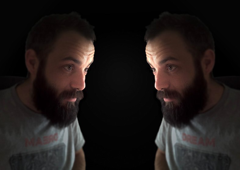 The performer of EDIT facing his own recorded image, two profiles lit against black