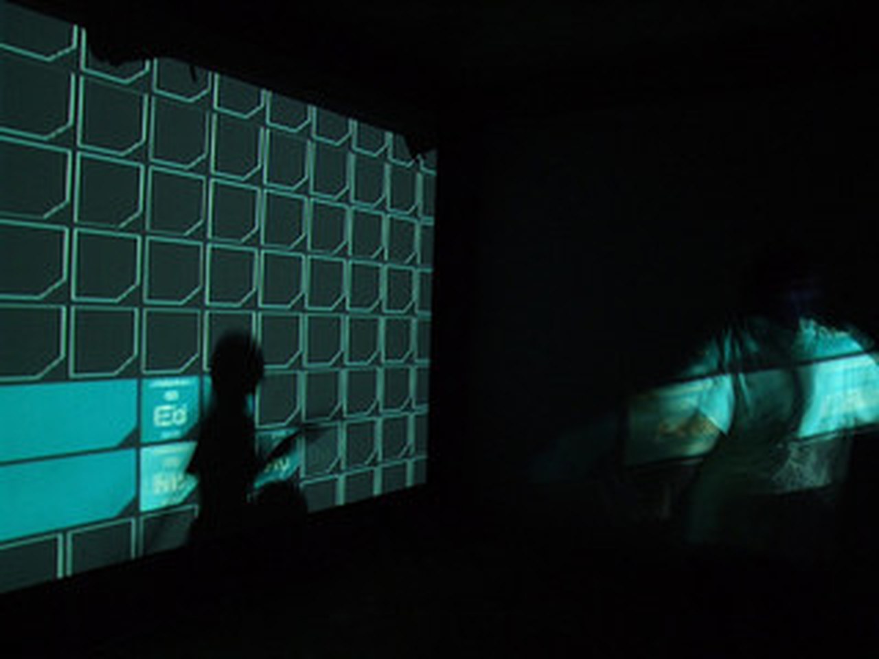 The empty grid projected on a wall in the dark, with one silhouette in front
