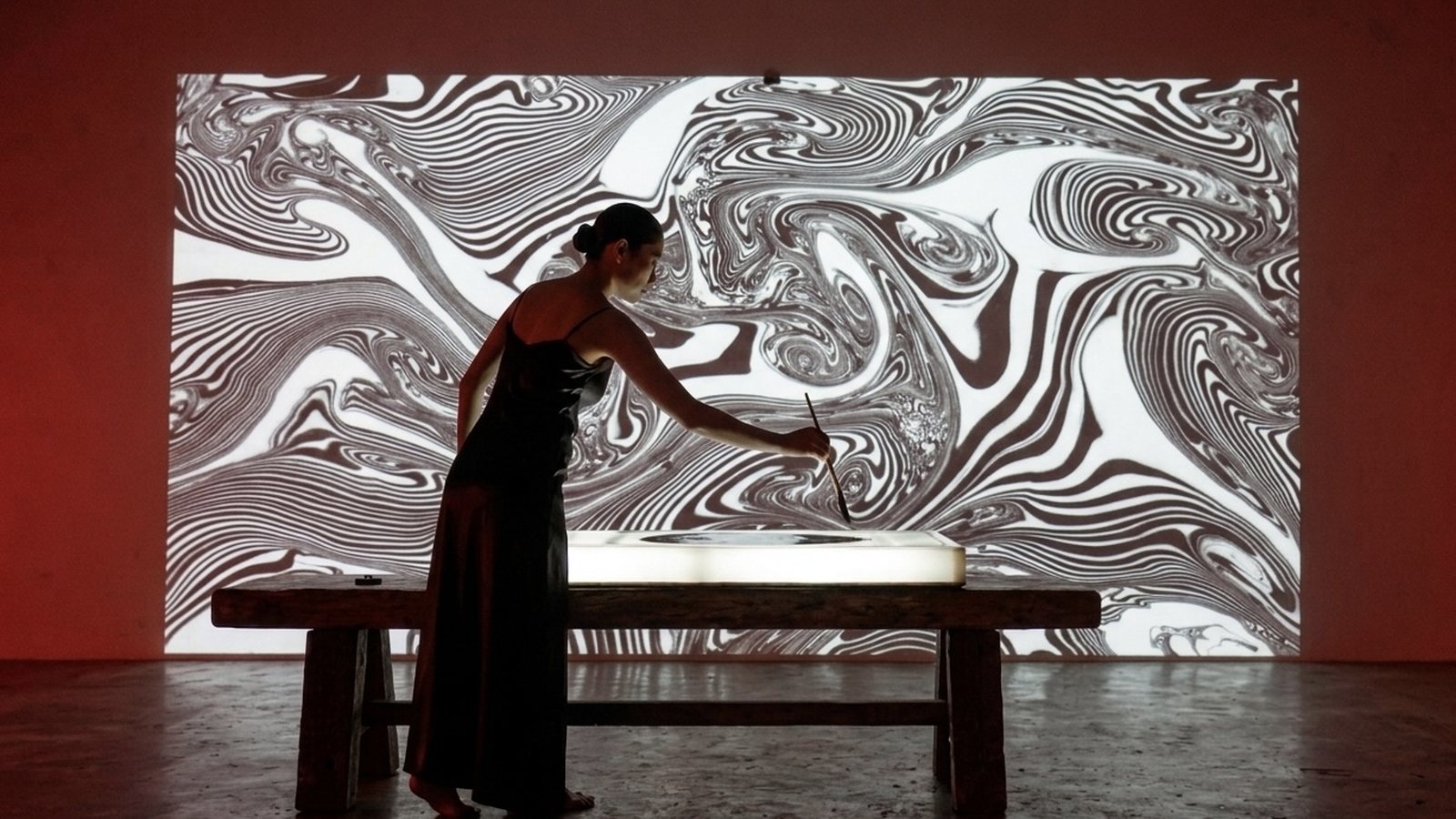 Concept visual: a woman painting at a lit table in front of a wall-sized projection of black and white marbling