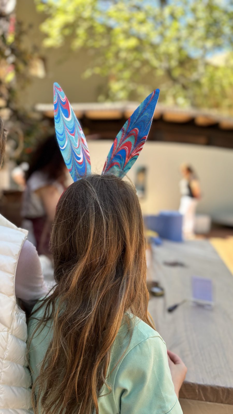 A girl from behind wearing marbled paper bunny ears in blue and red, at the Costa Navarino workshop