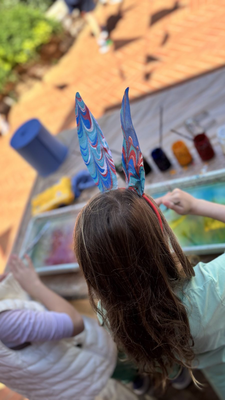 Seen from above: a girl in marbled bunny ears leaning over a marbling tray