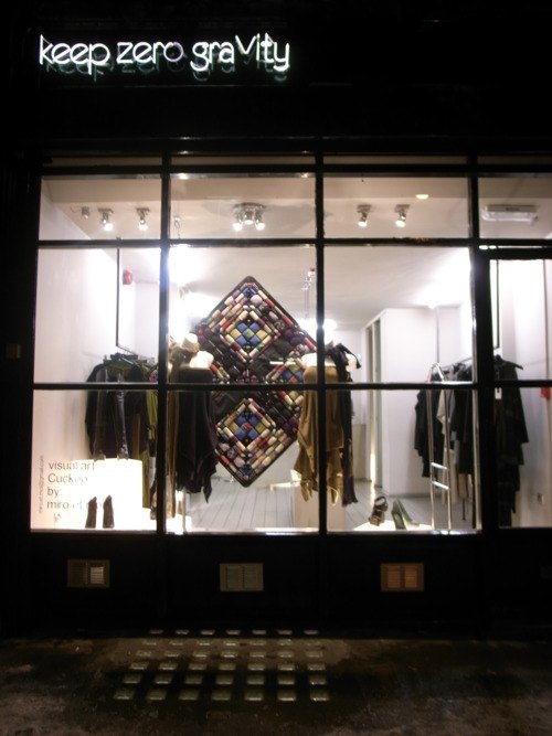 The shop window at night, with clothes and a diamond-shaped textile work