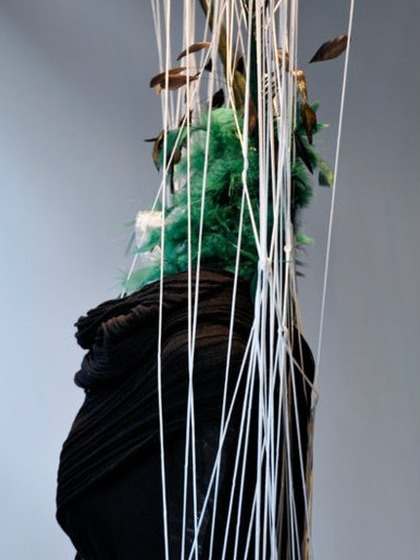 Detail of a window display: a mannequin with green feathers and pale strands